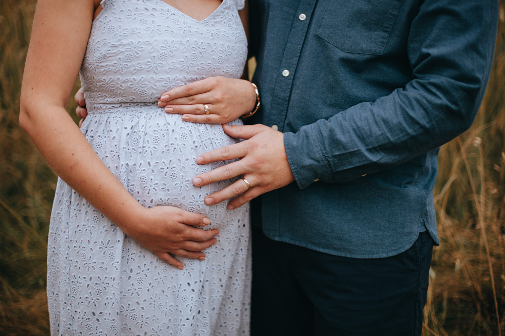 Schwangere Frau und ihr Mann halten Hände an ihren Babybauch